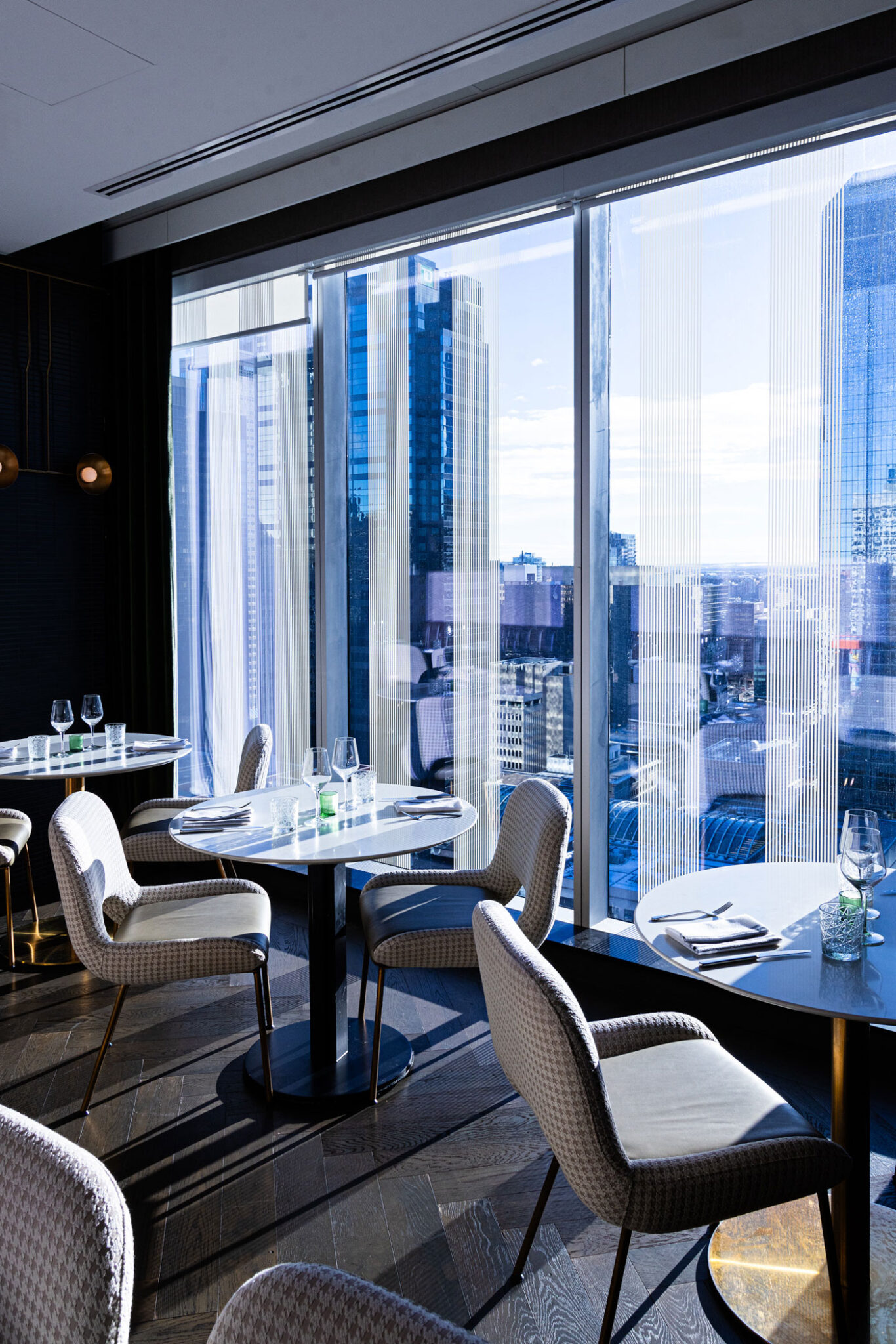 A restaurant interior with chairs and tables and office towers outside the windows.