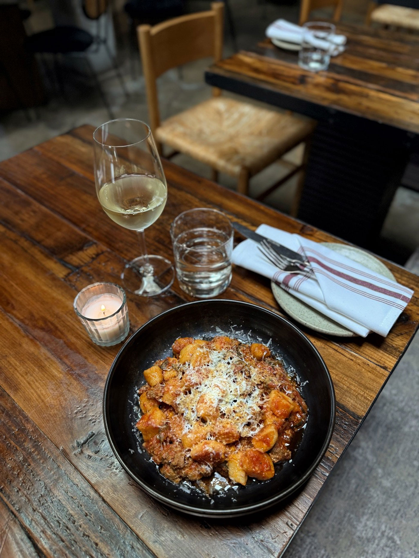 A bowl of pasta and a glass of wine sit on a restaurant table