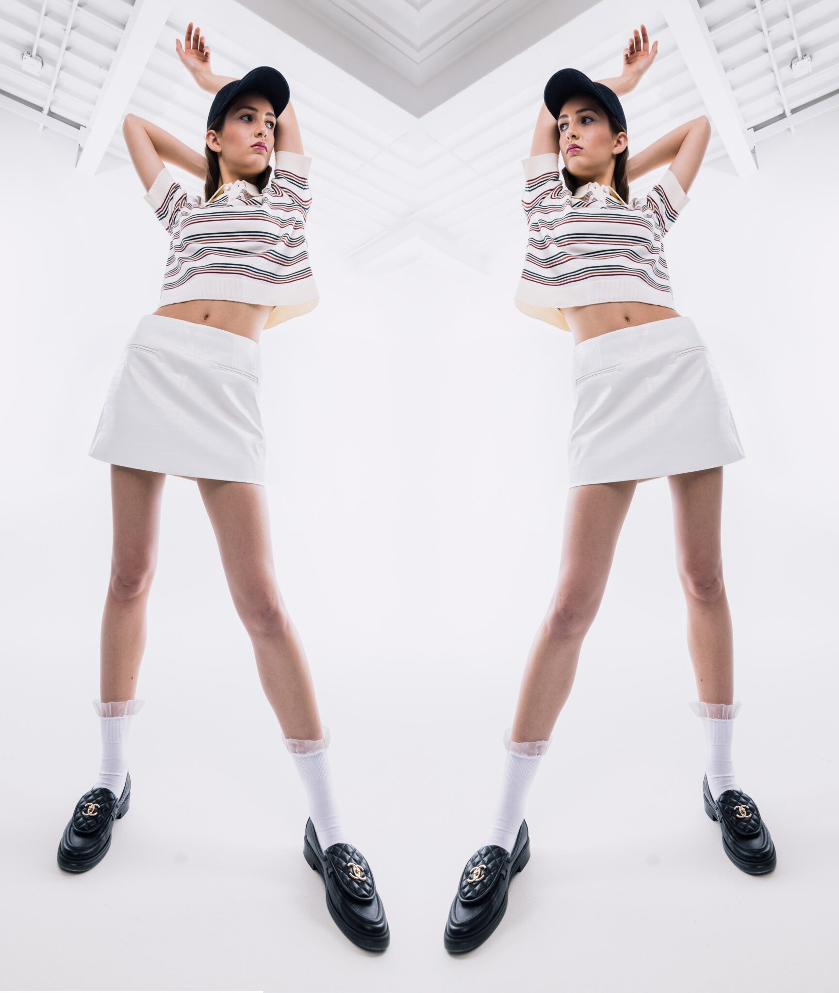 A model mirrored wearing a hat, a cropped top, skirt and loafers. 
