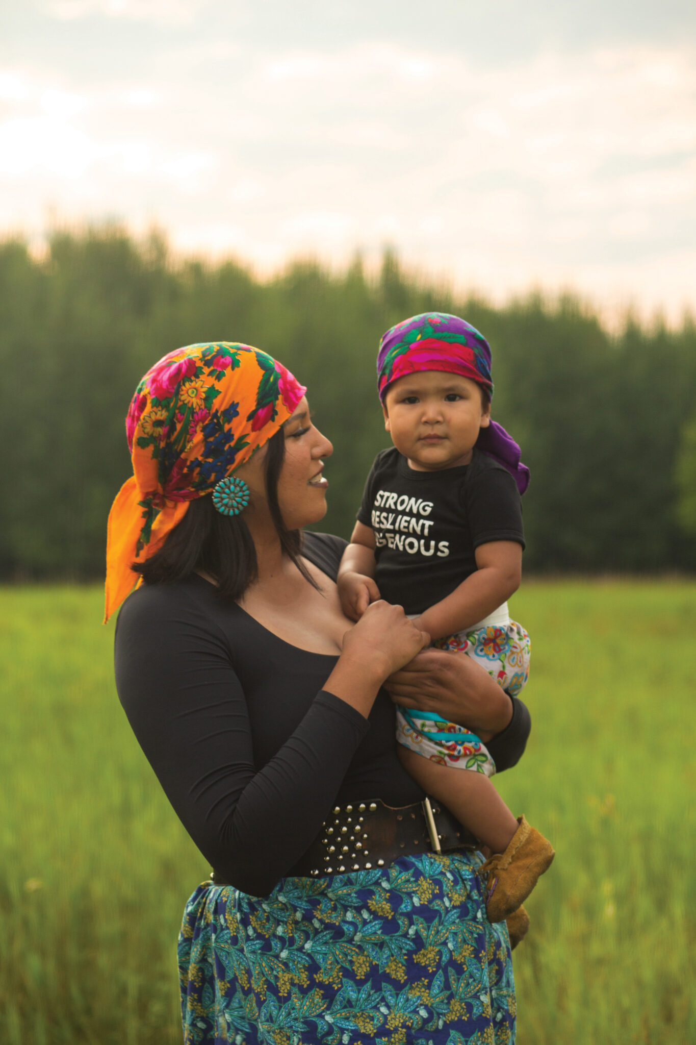 Alanna Bluebird holding her daughter in a field.