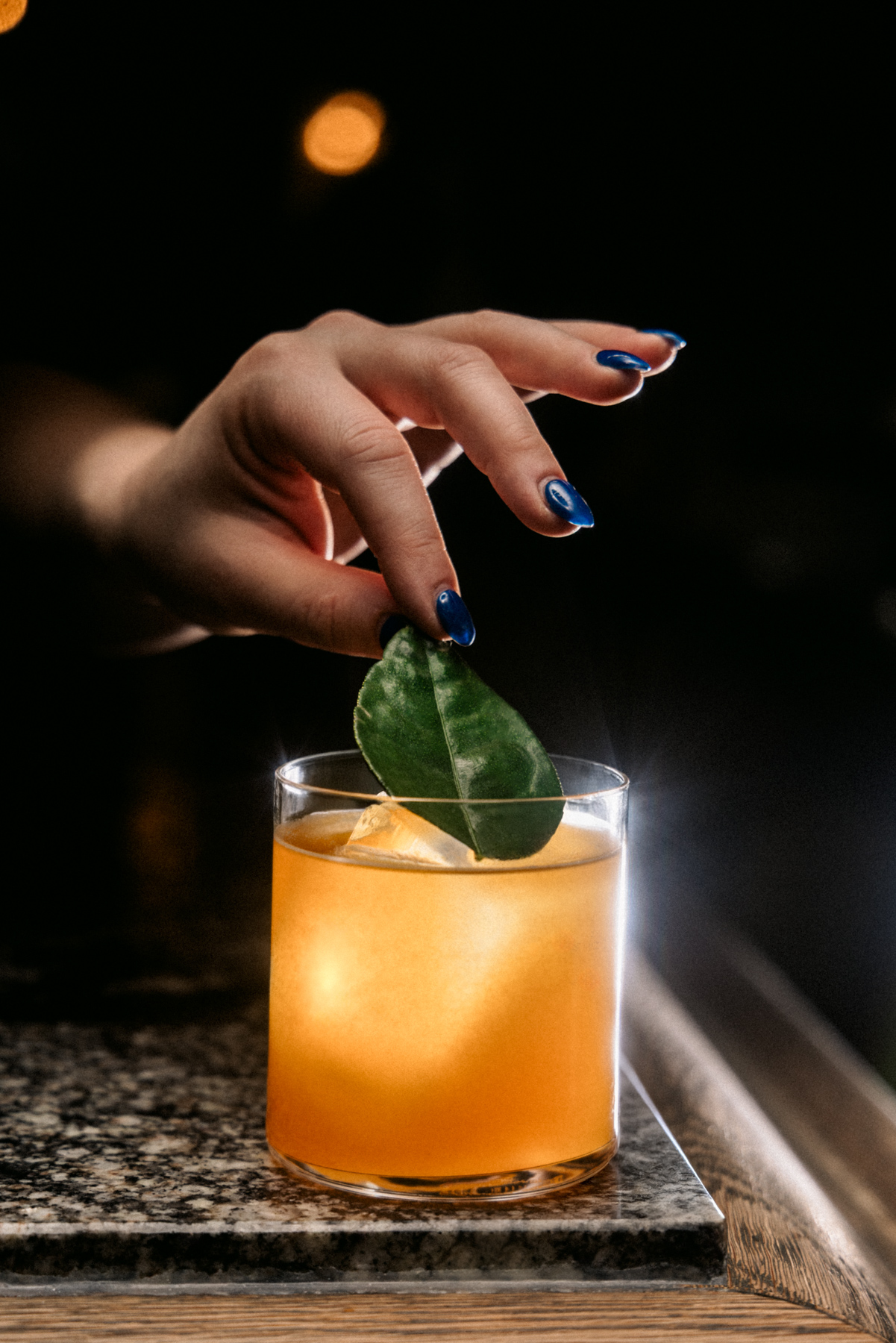 A hand places a leaf on top of a non-alcoholic beverage. 