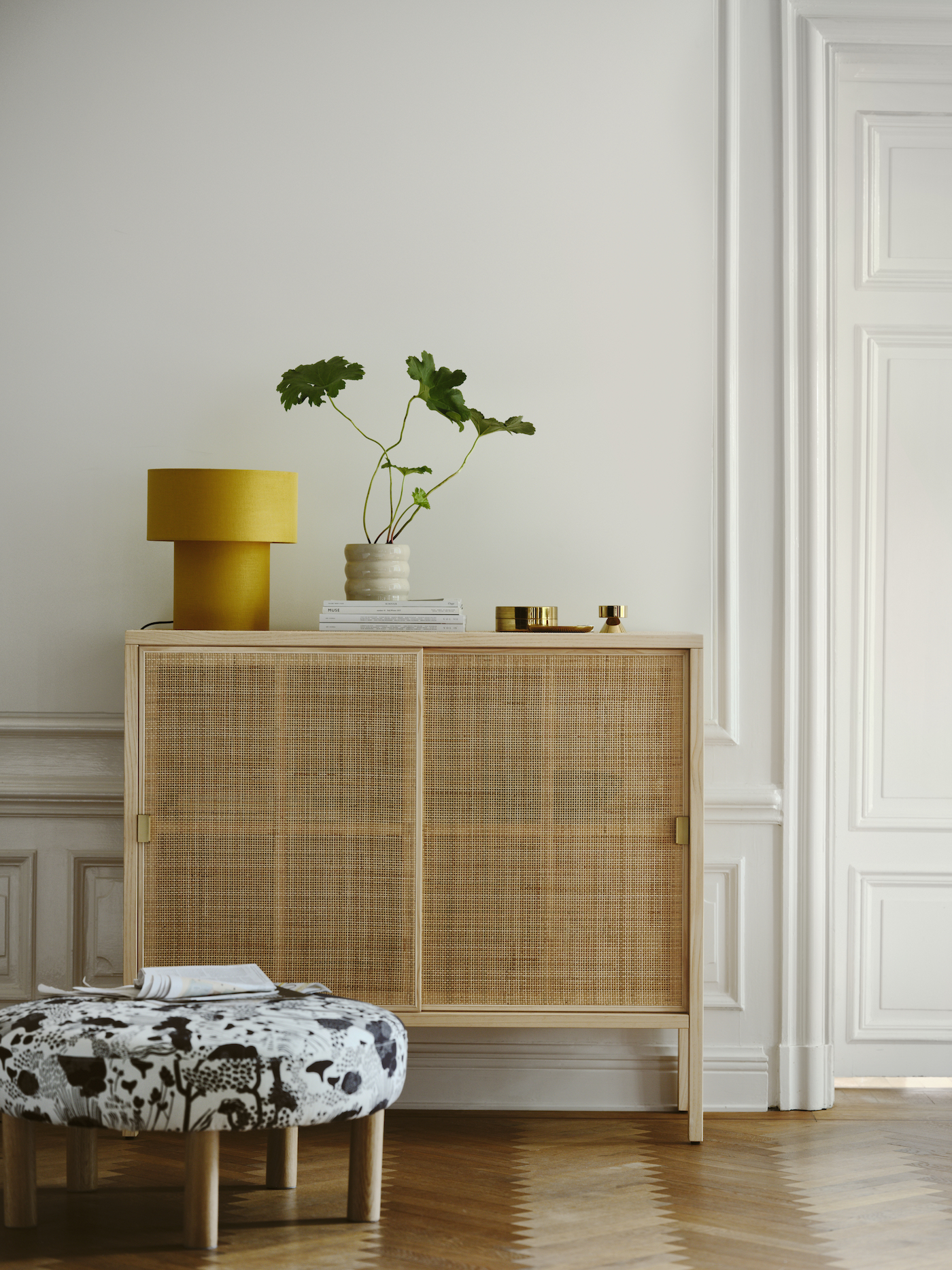 A rattan cabinet with a yellow lamp and a plant sitting on top.