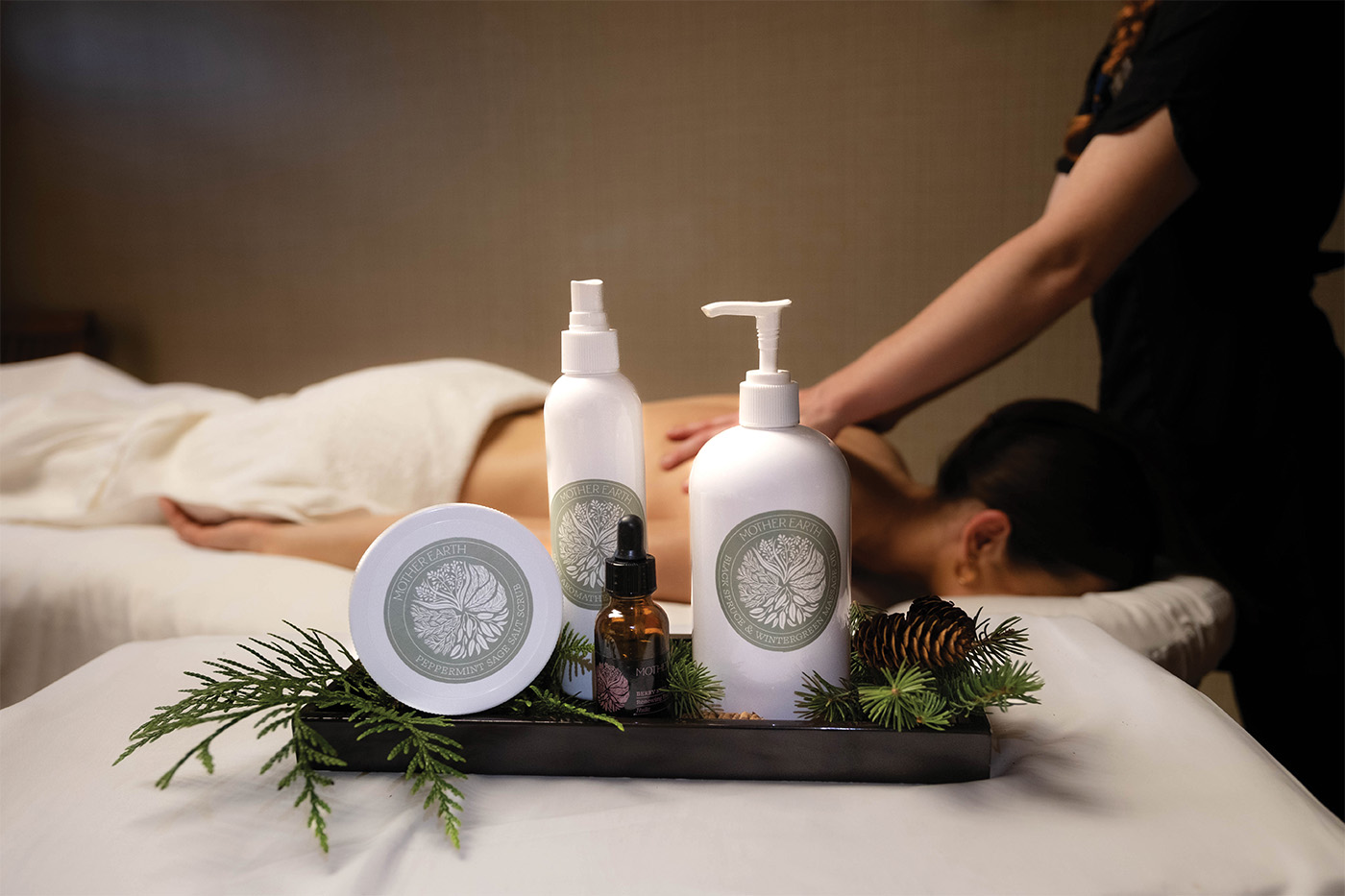 A woman getting a massage in the background with Mother Earth Essential products in the foreground.