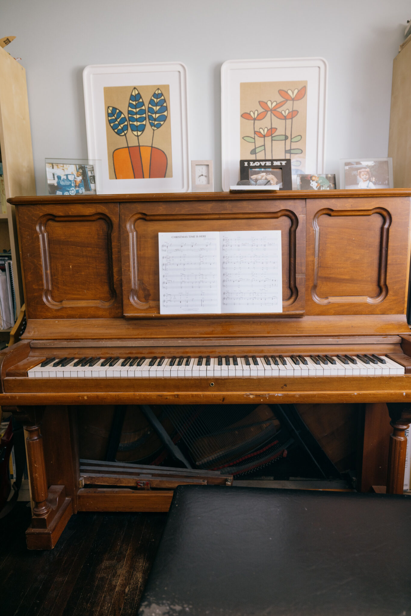 A wooden piano with framed photos and images sitting on top of it