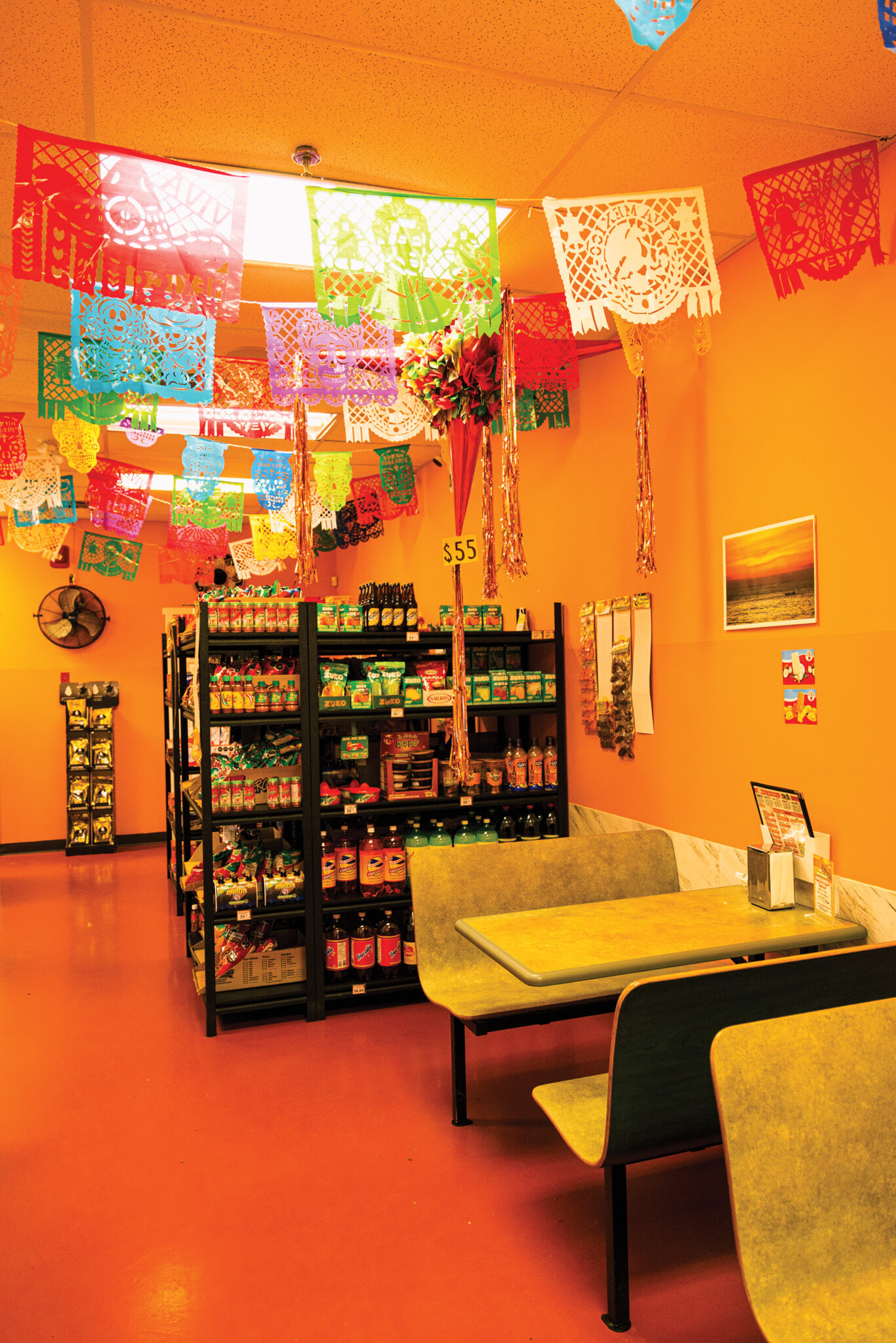 A Mexican restaurant with a bright orange interior, seating and shelves with food products.