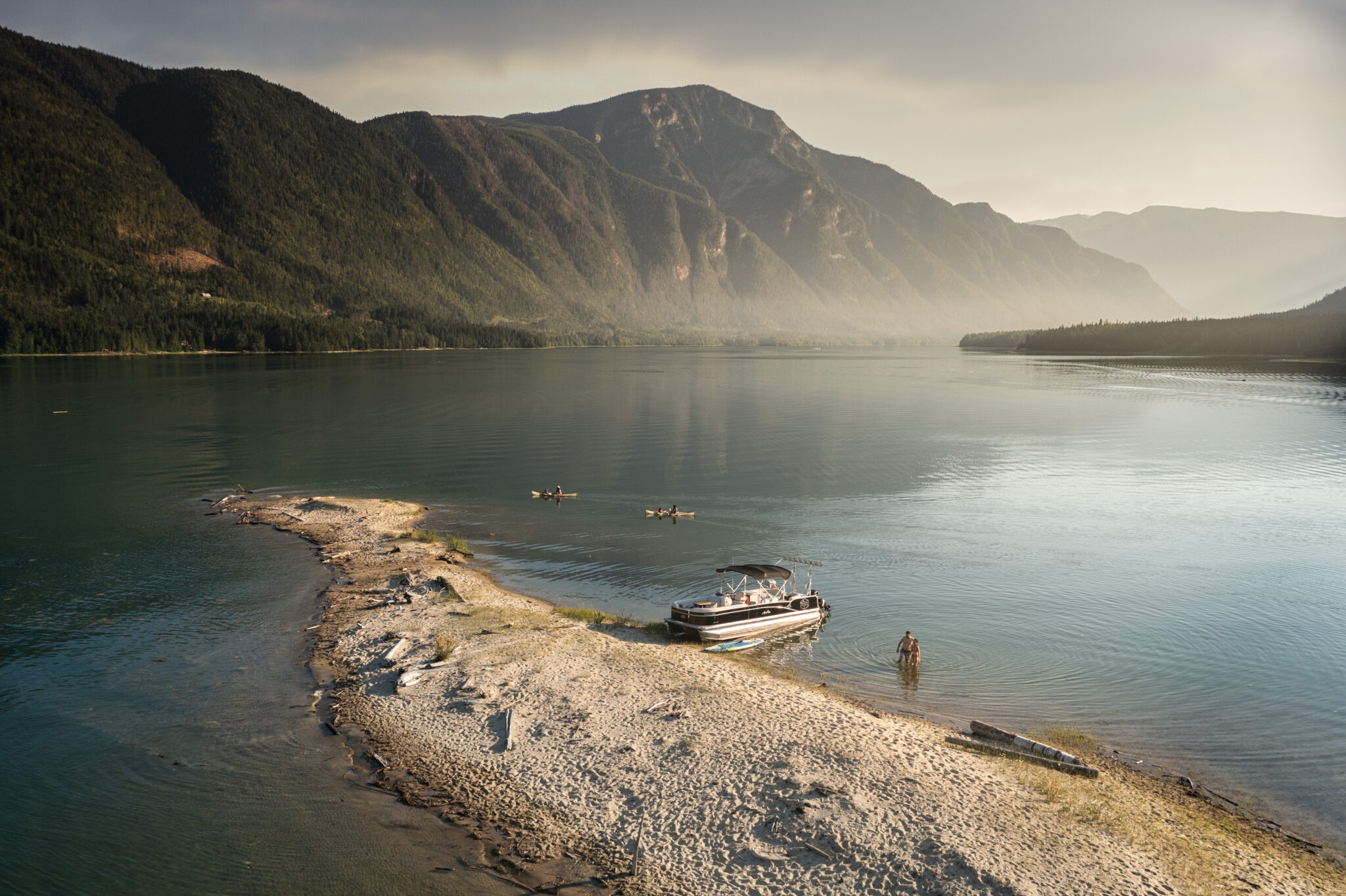 A boat docks on a small sliver of land with mountains in the background.