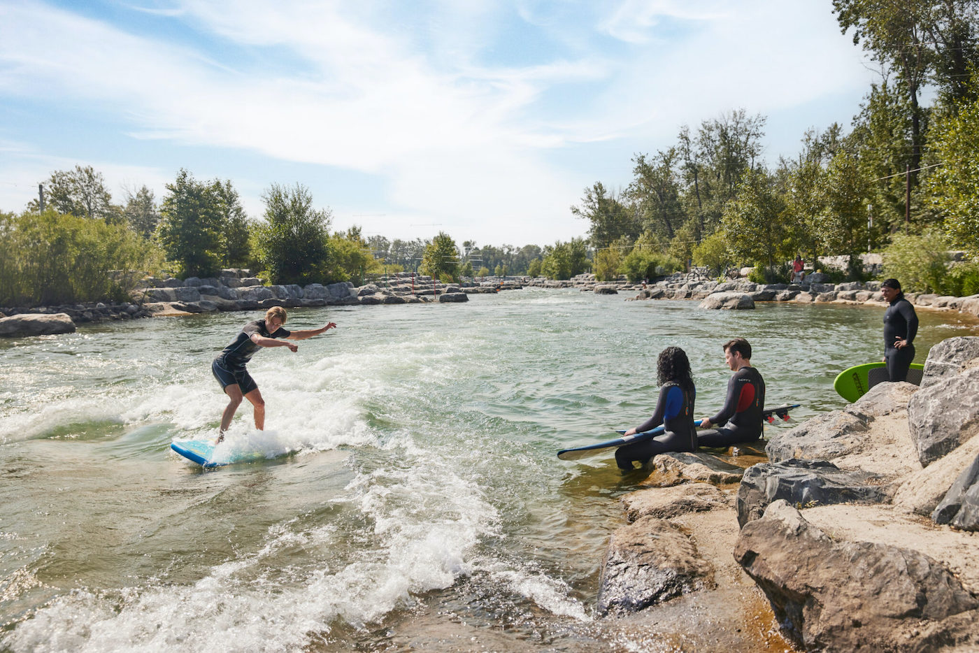 A man surfs on the river as three friends watch.