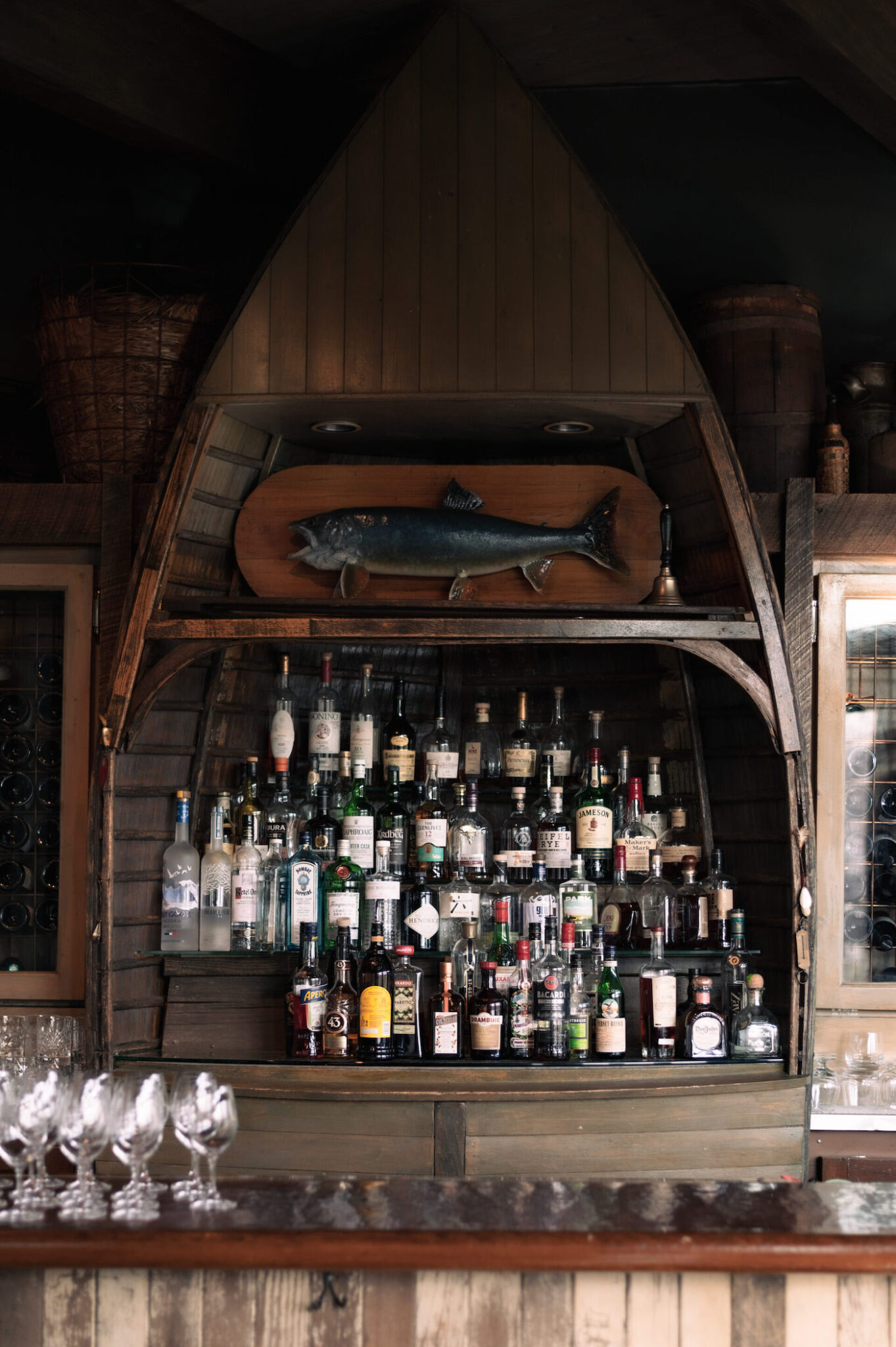 A restaurant bar shelf filled with various liquor bottles with a decorative fish above. 