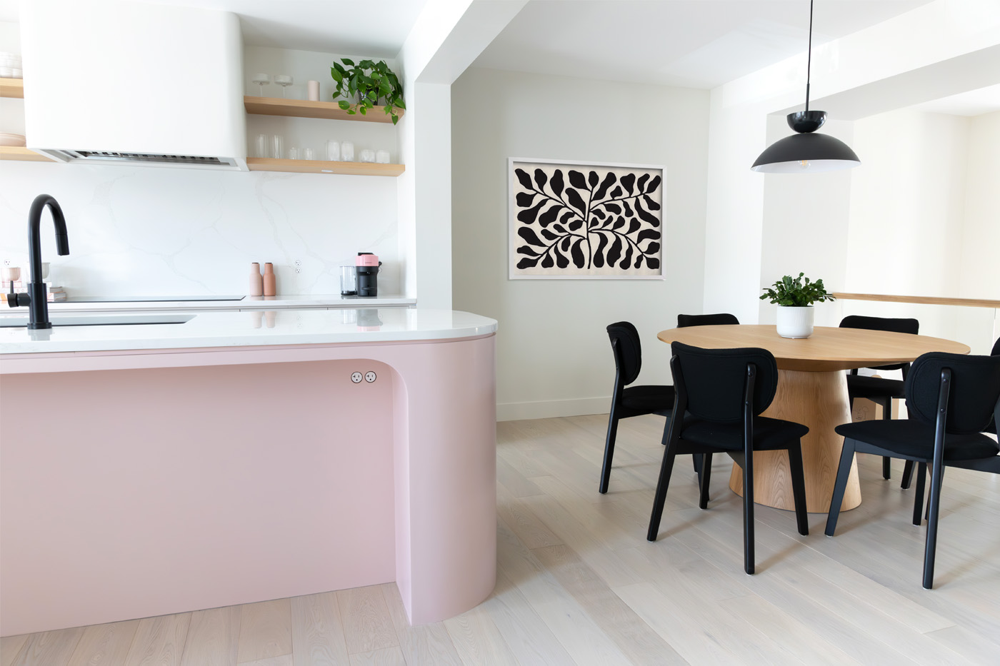 A kitchen with a blush-toned island, black dining chairs and wood table.