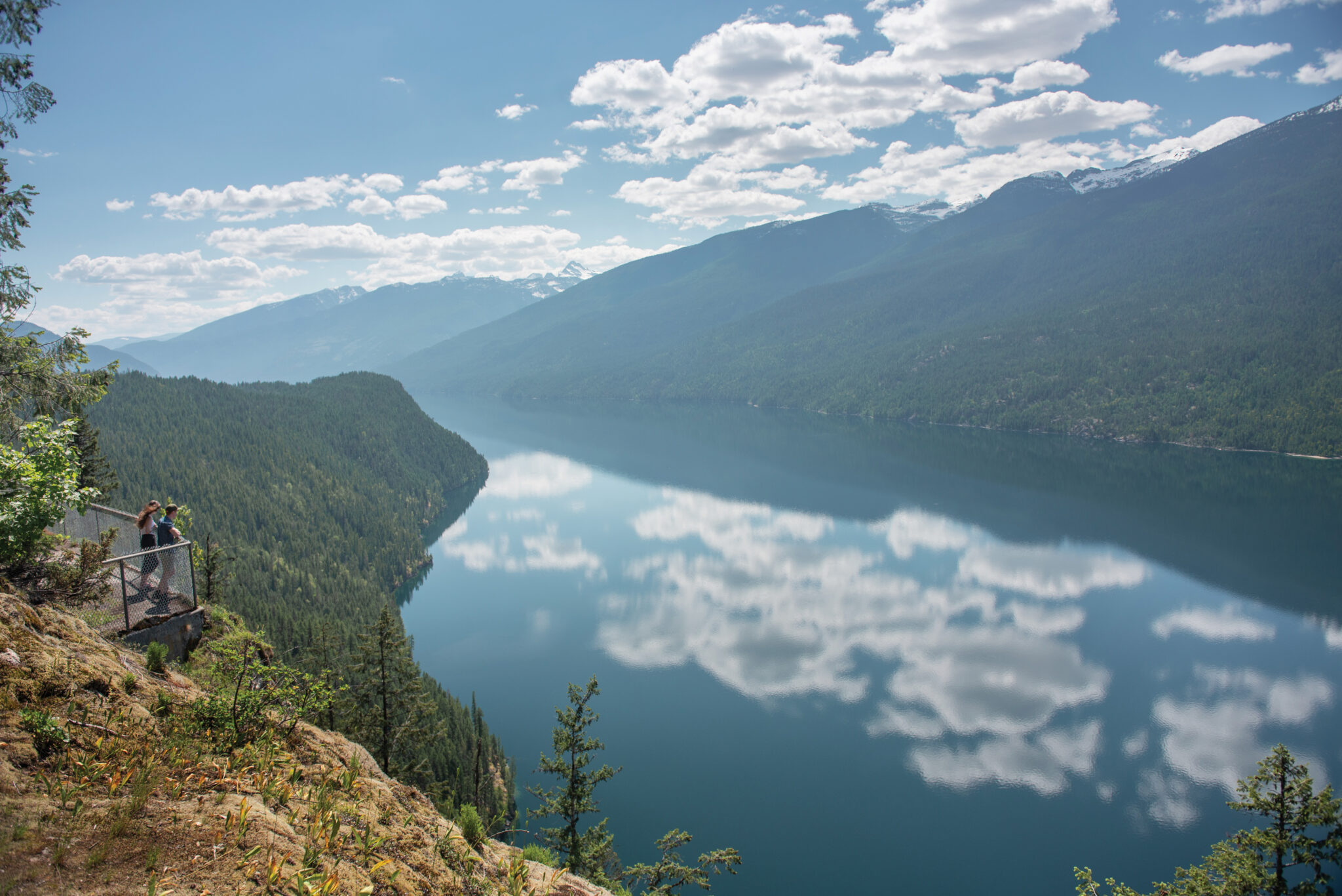 A lookout spot overlooks a beautiful landscape with a lake surrounded by mountains.