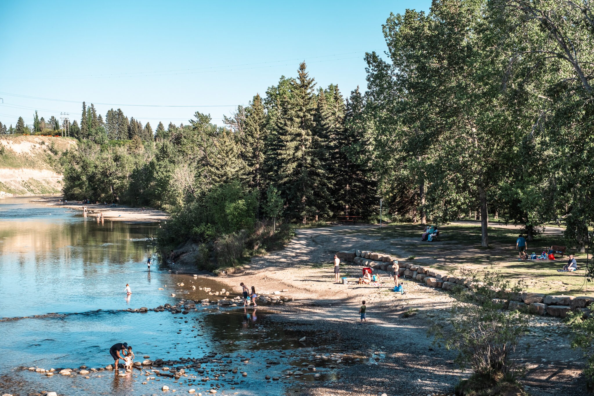 People hanging out in a beach area with water, sand and trees.