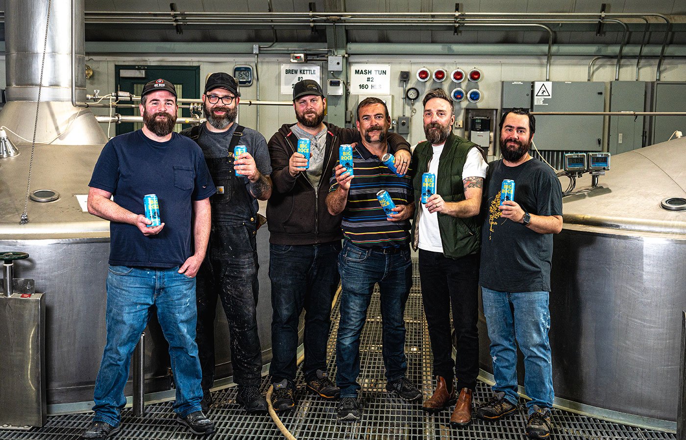 Six men stand beside brewing equipment inside of Big Rock Brewery.