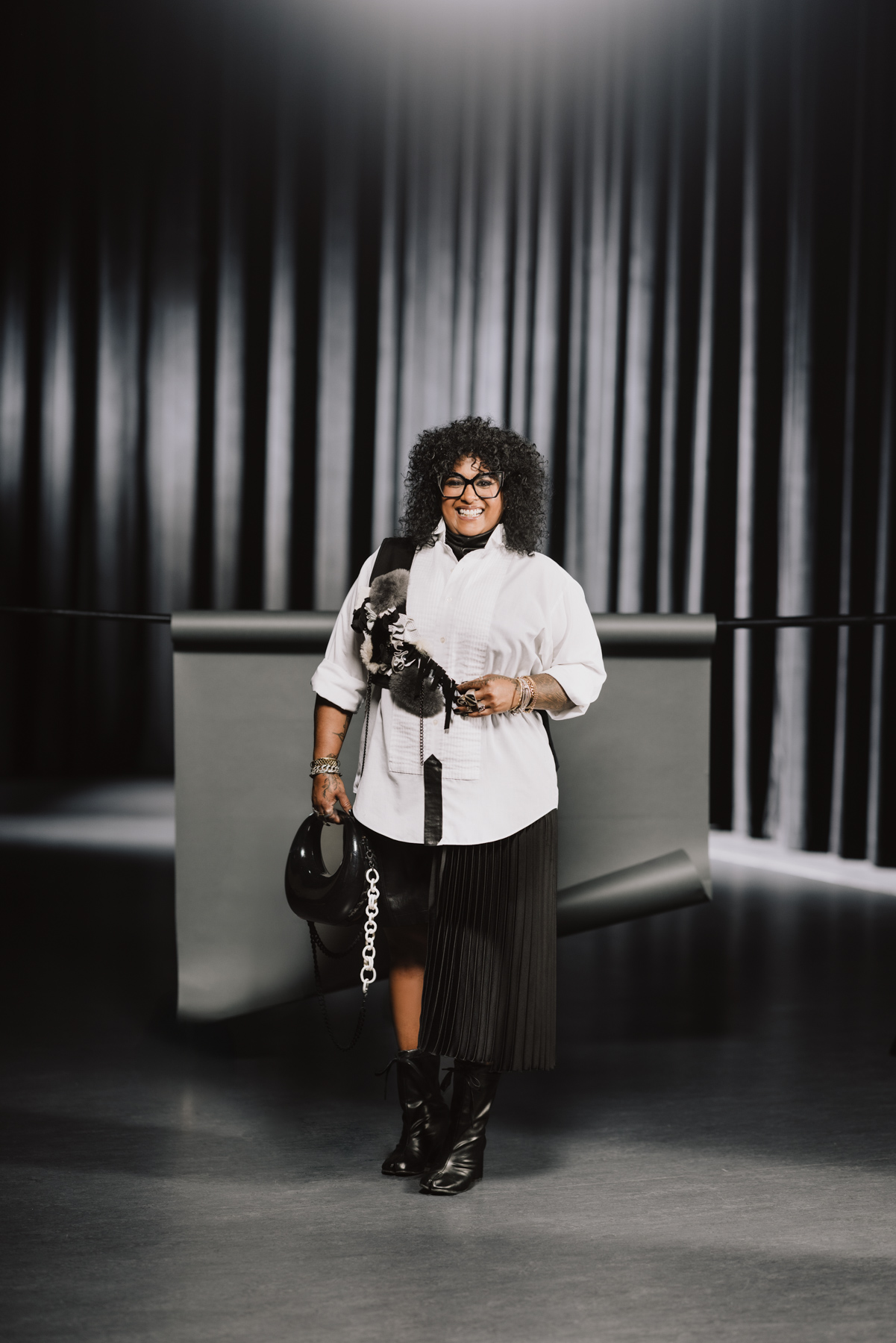 Leela Jacobs wears a white button shirt, black shorts and skirt, black boots and a purse.