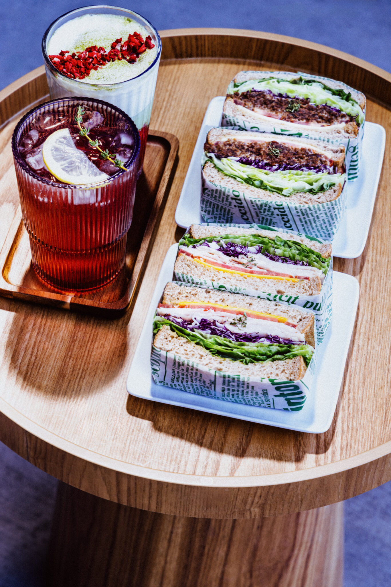 Two plates of cut sandwiches and two beverages sit on a table.