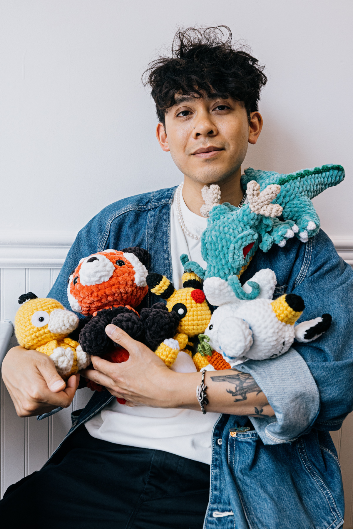 A man sits holding colourful crocheted animal figures.