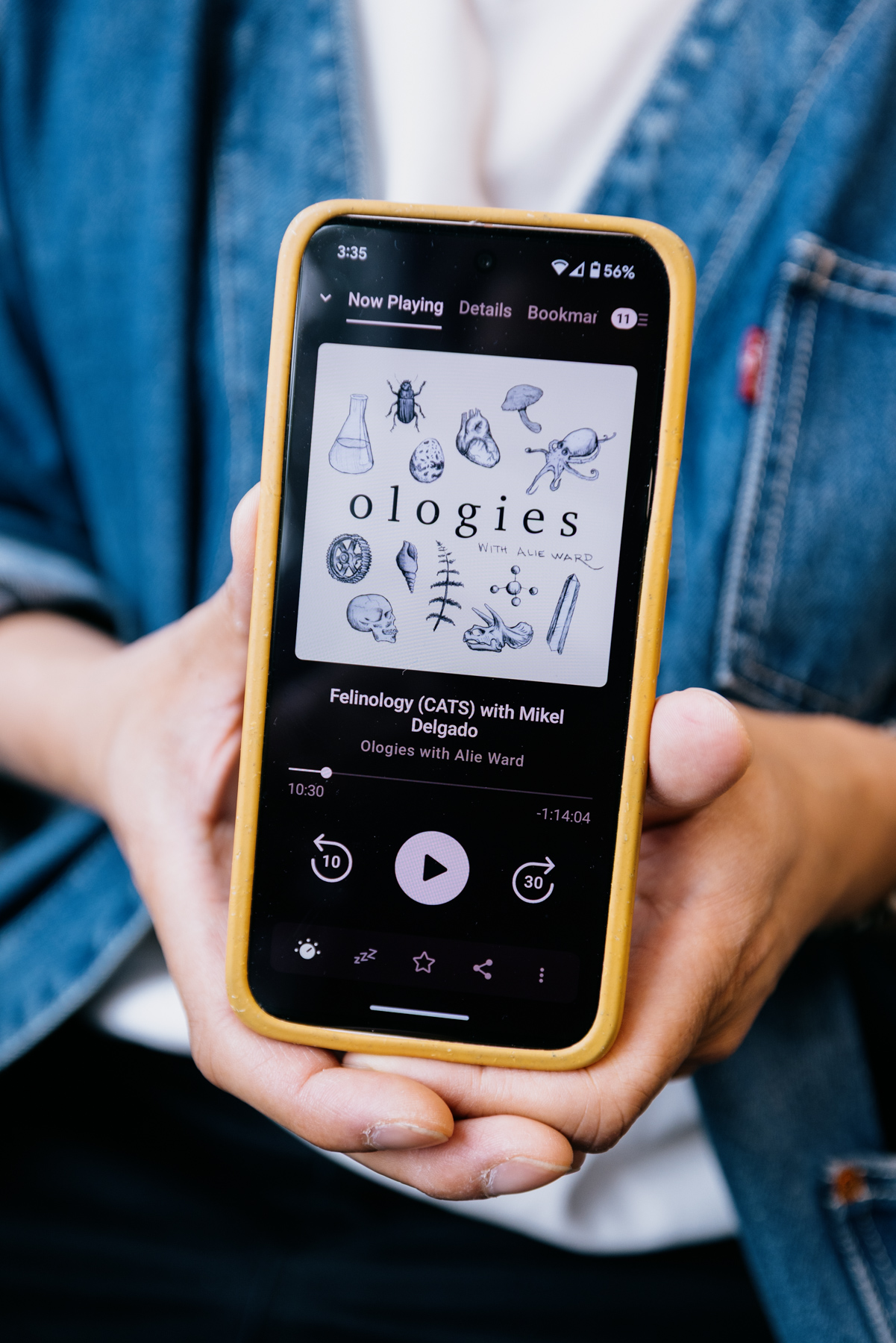 Two hands hold up a phone that is open to a podcast
