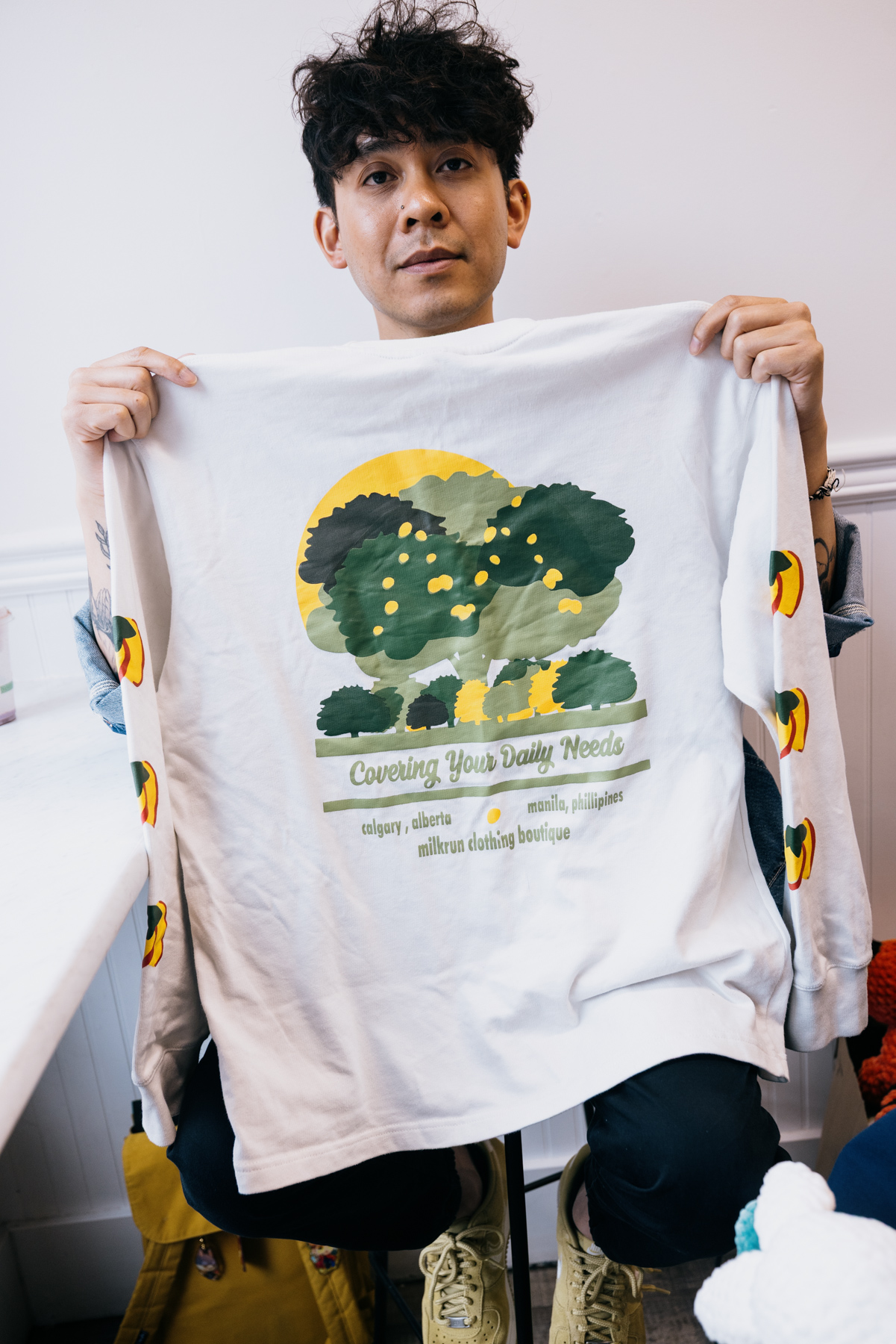 A man holds a graphic t-shirt with trees and lemons on it.