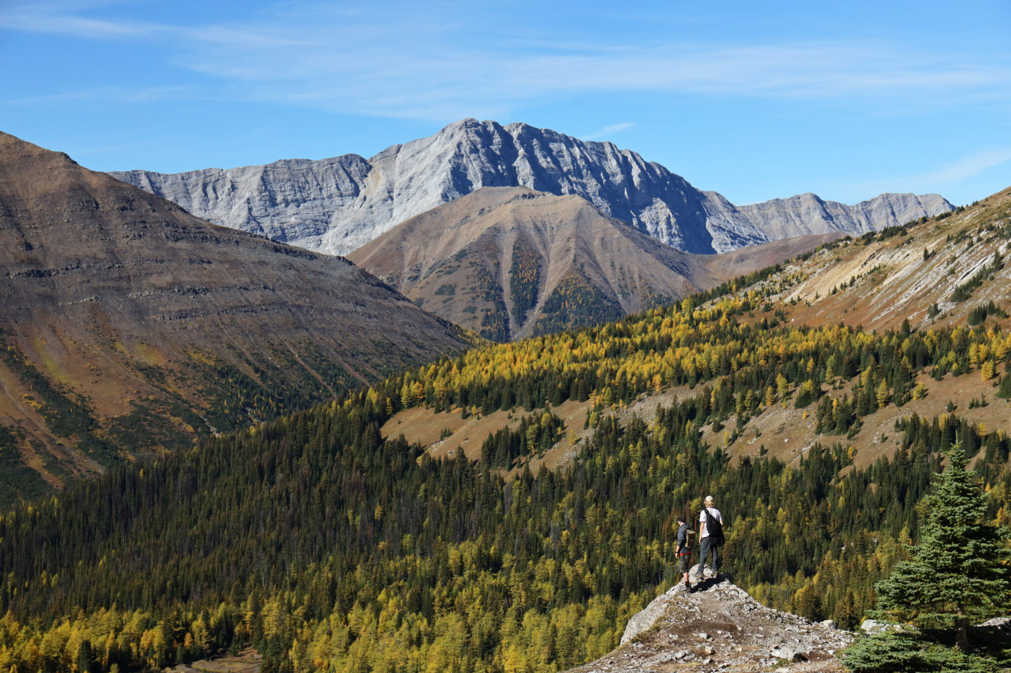 Two people stand at a lookout point overlooking a mountain range.