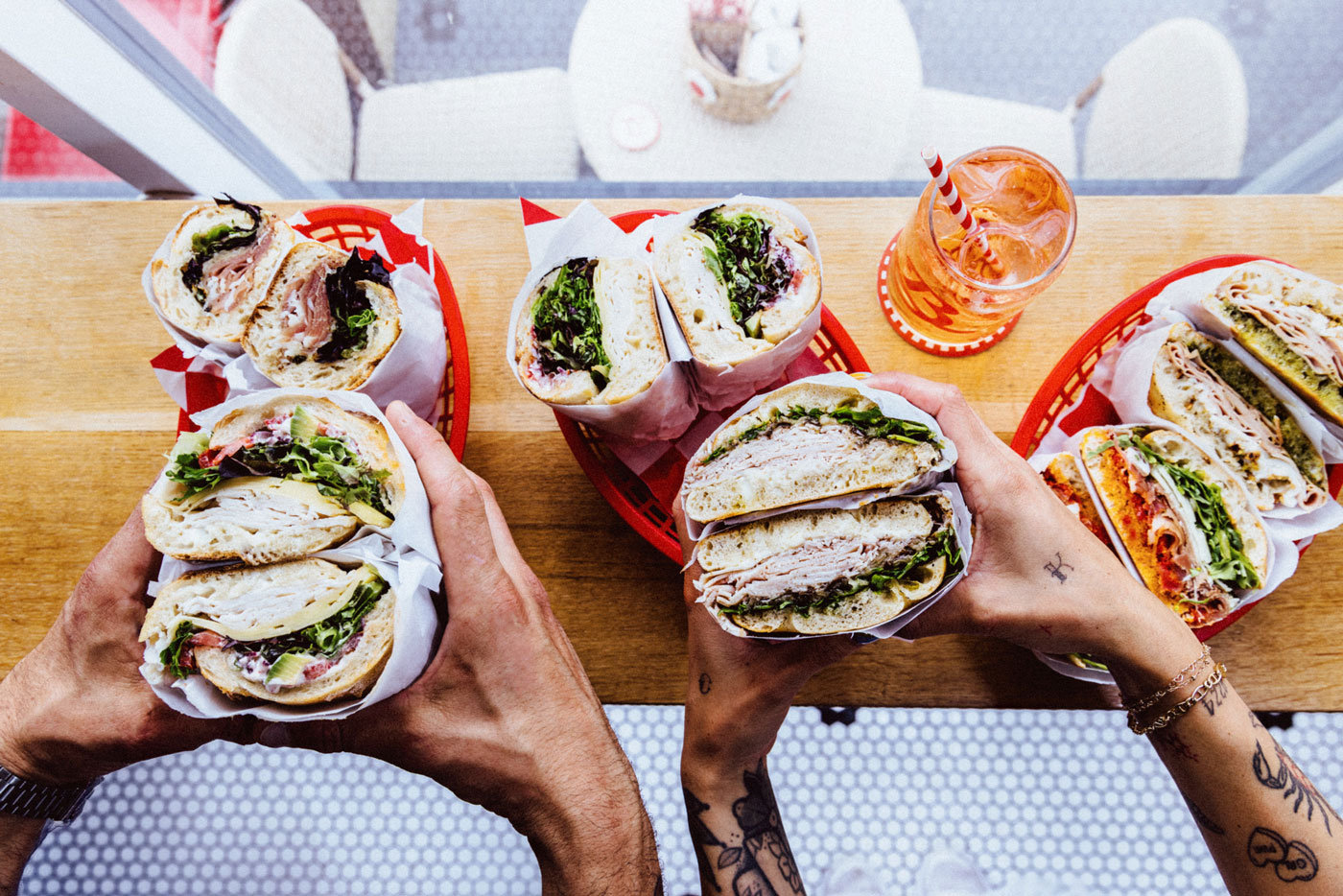 An overhead view of two sets of hands holding sandwiches cut in half. 