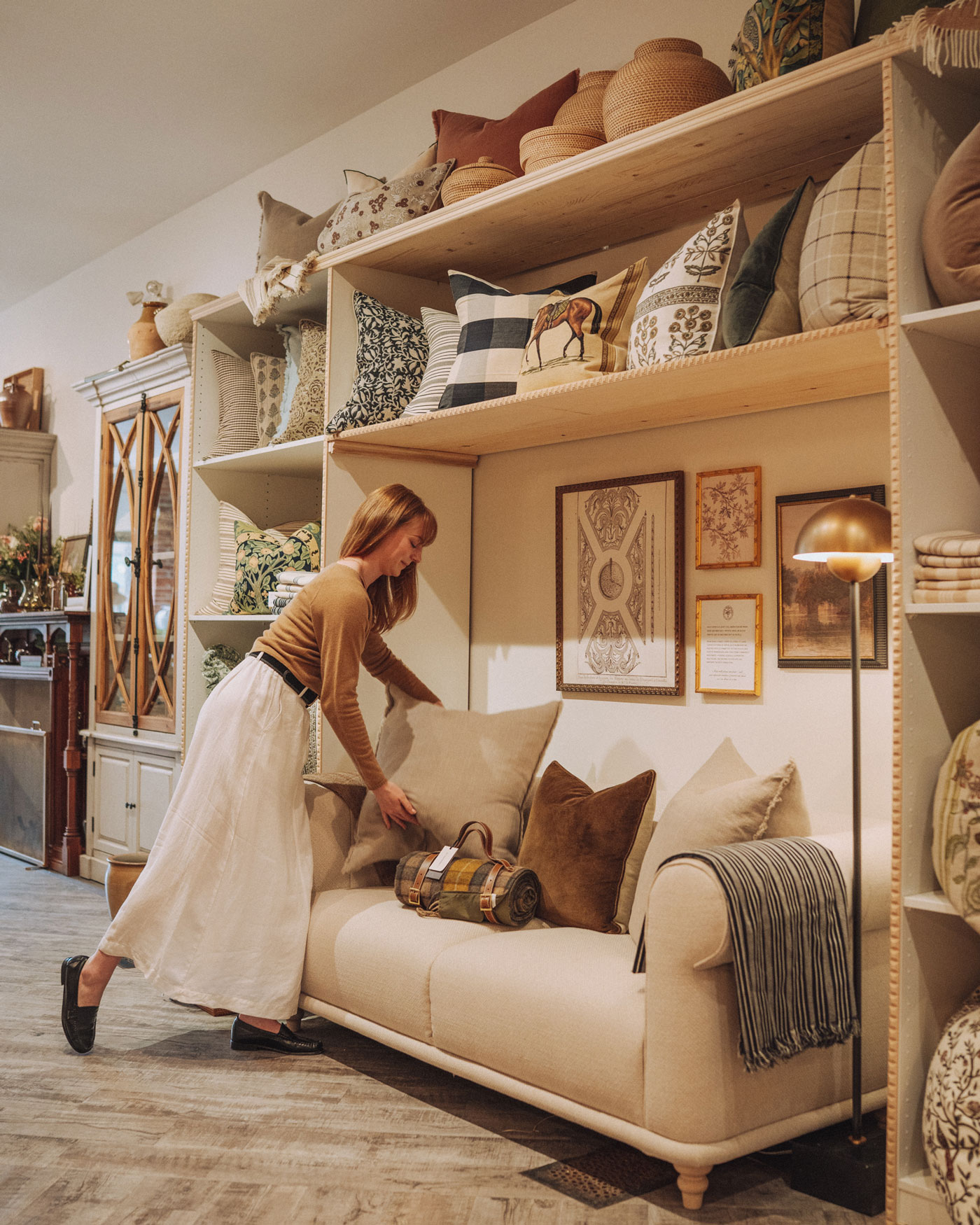 A woman arranges a pillow on a couch in a store display