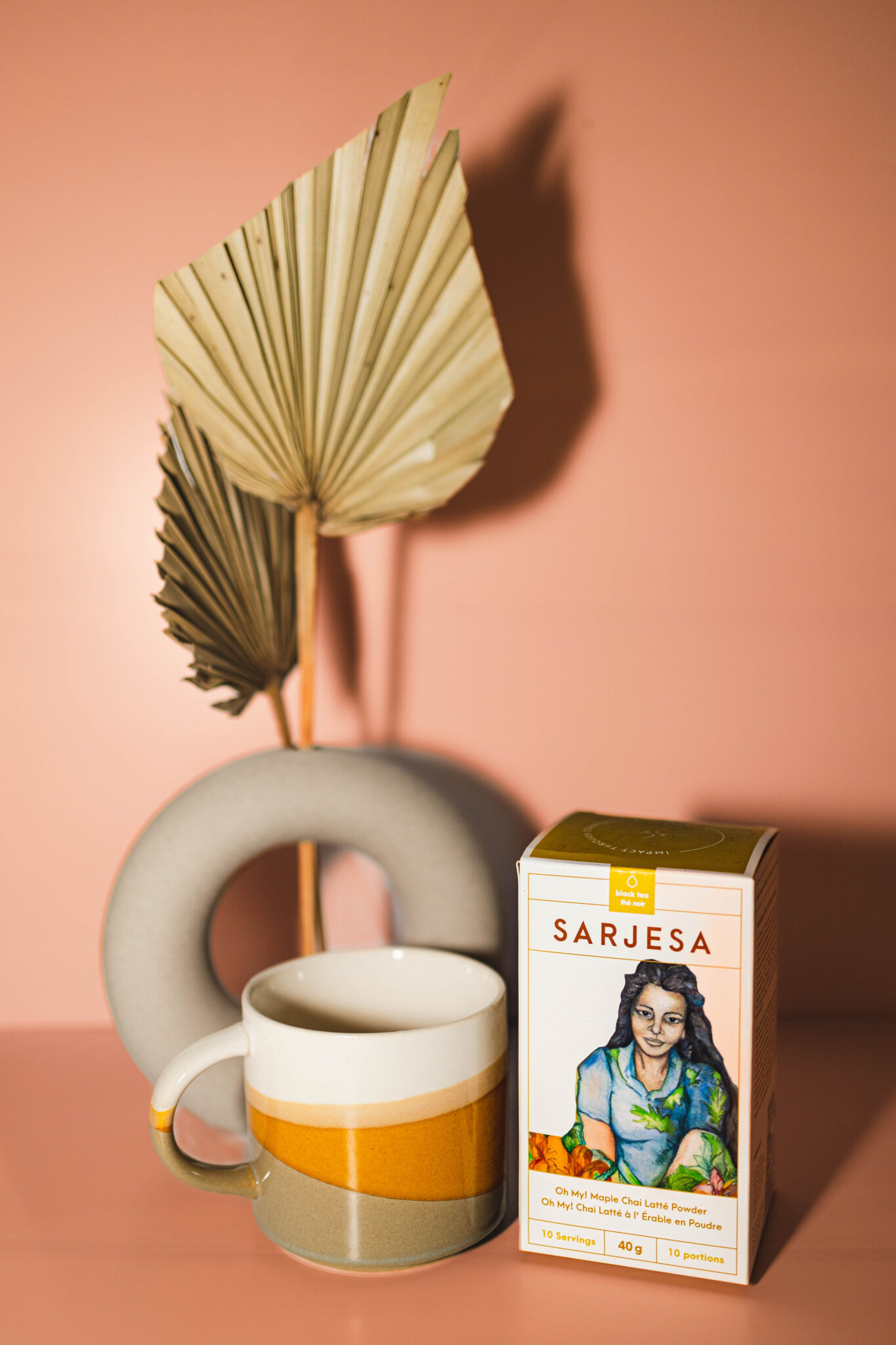 A colourful mug beside a box of tea with a circular decoration in the background.