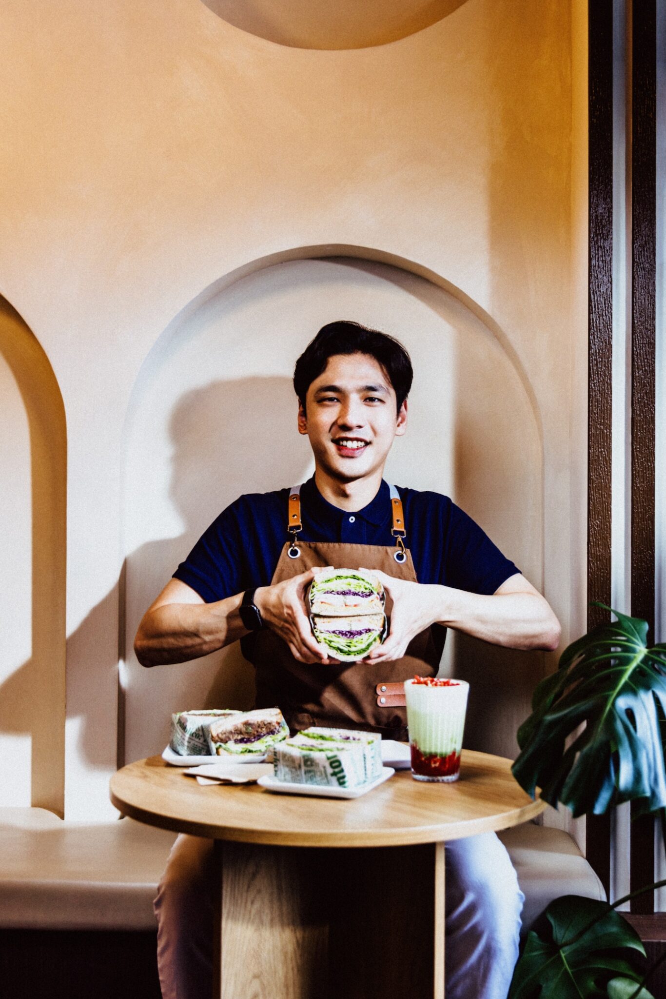 A person sitting behind a table holds a sandwich open 