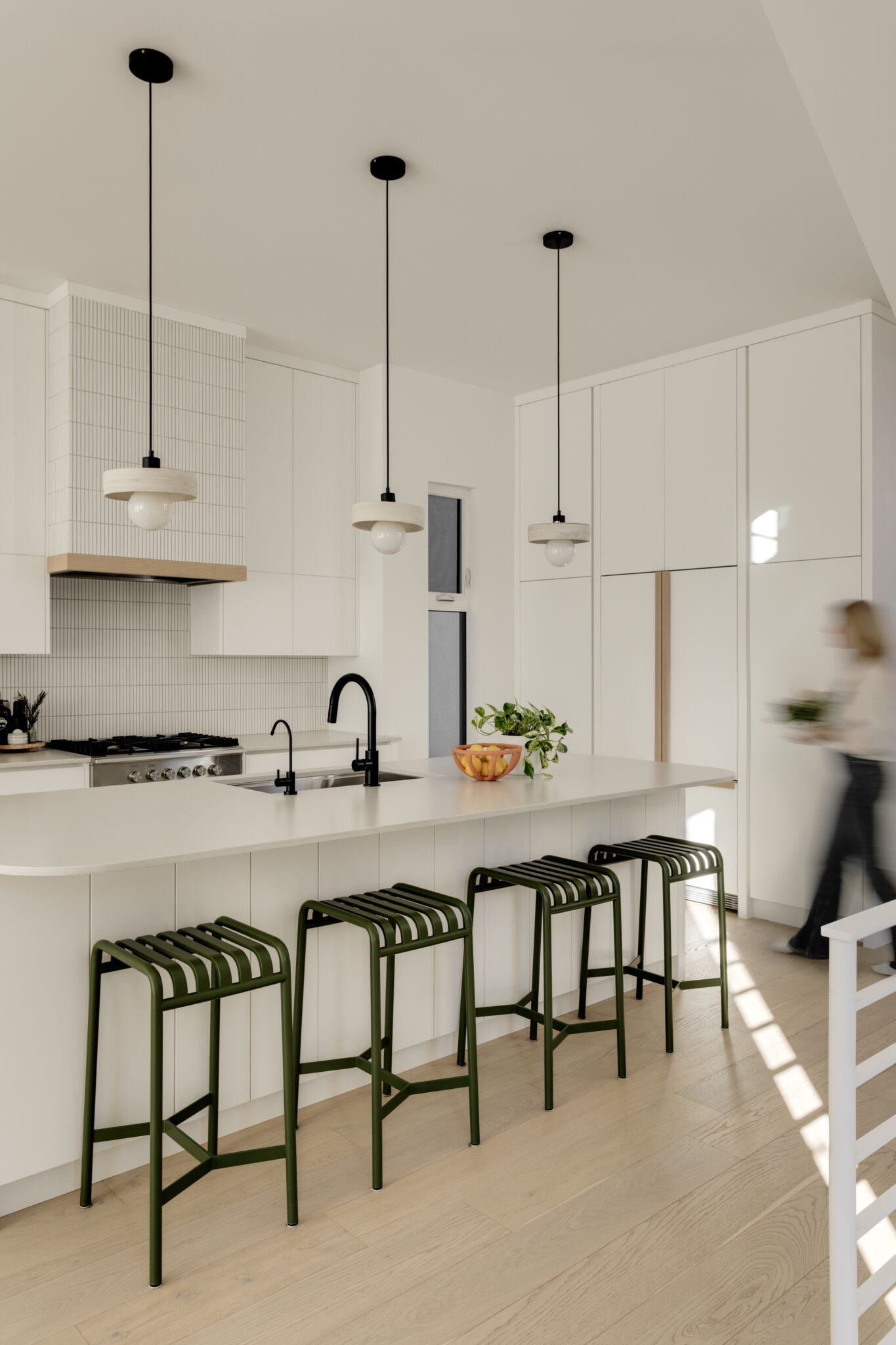 A blurry figure walks through a home kitchen with an island and green stools.
