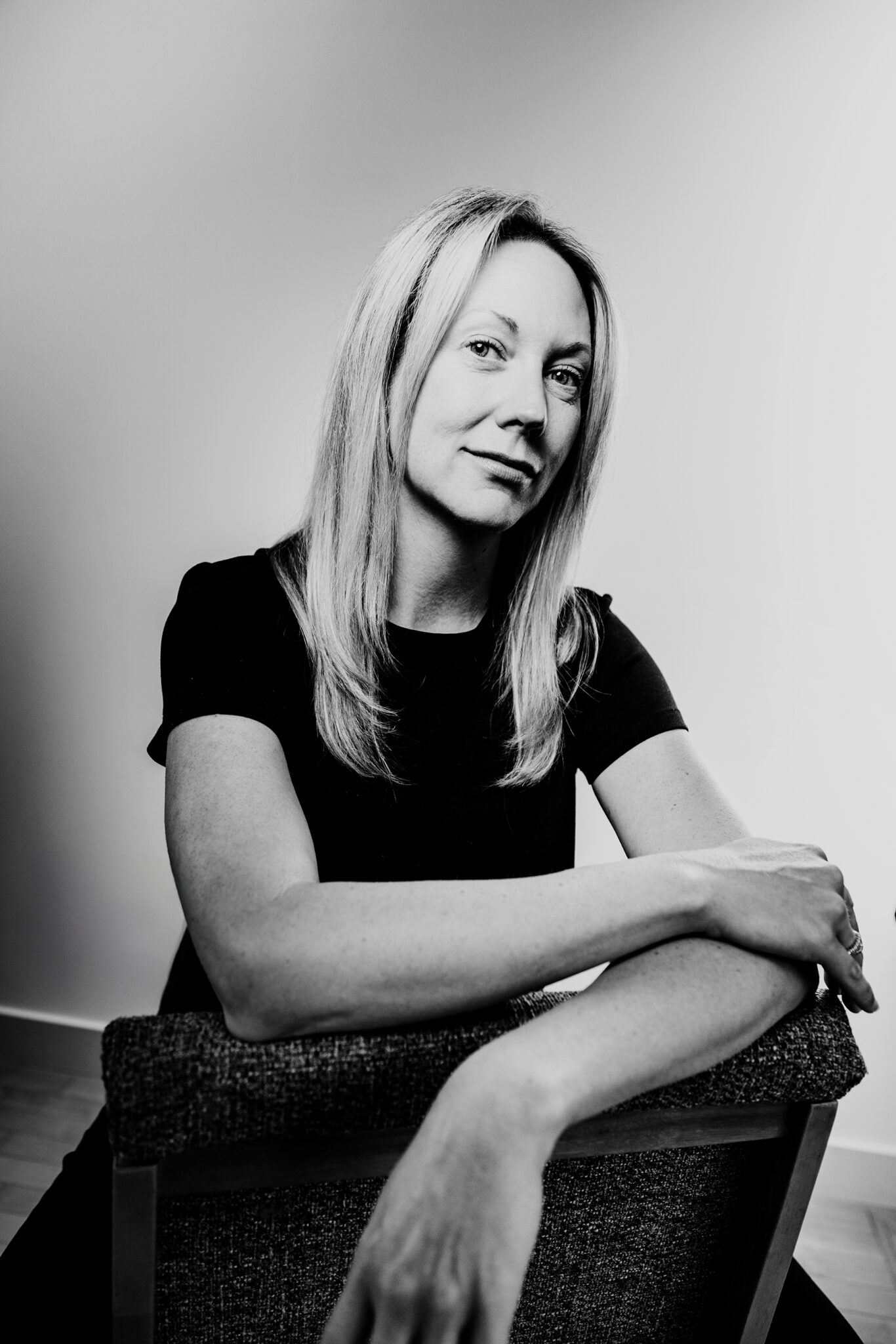 A black and white portrait of a woman sitting with her arms crossed over the back of a chair.