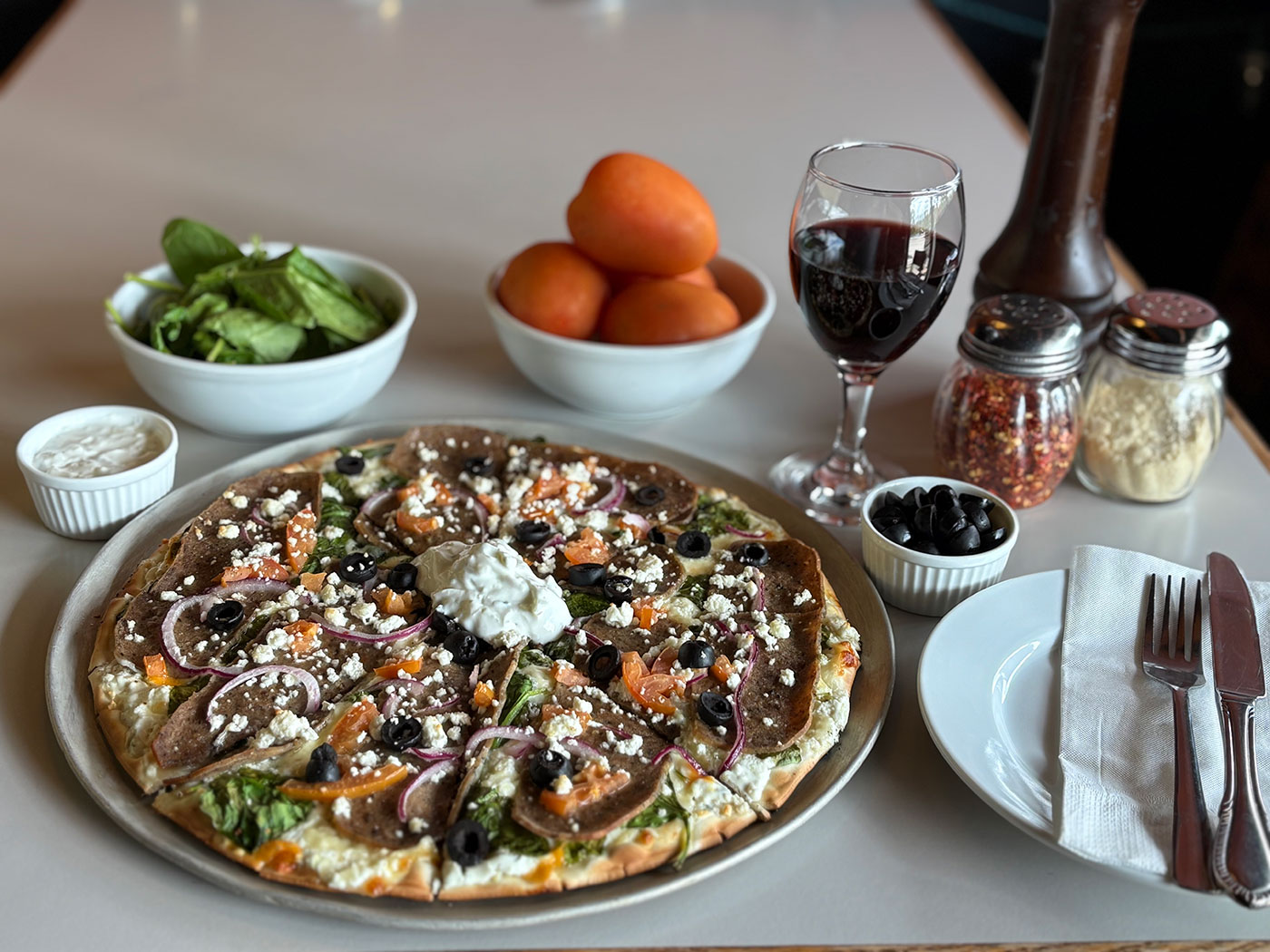 A pizza surrounded by ingredients and a glass of wine
