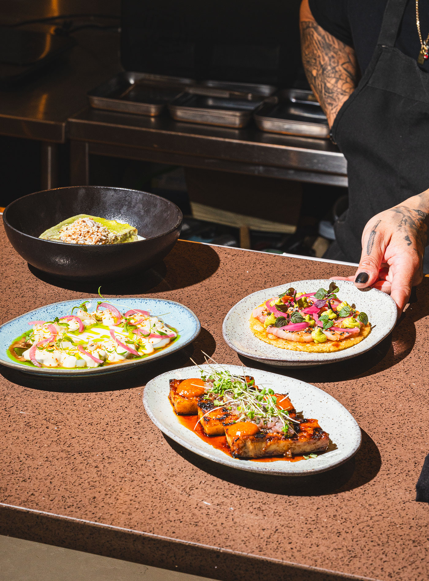 A variety of dishes available at Orijins, with a chef's hand placing one of the plates down.