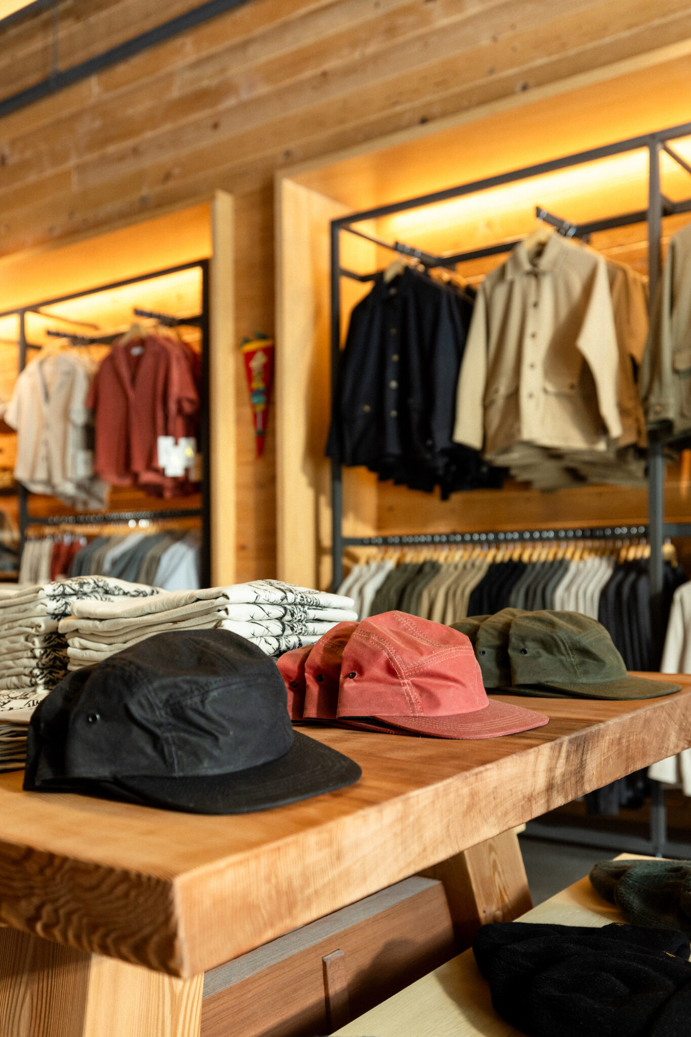 Hats sit on a display table in a store with jackets hanging in the background