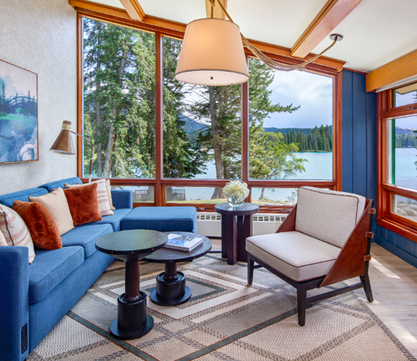 A hotel room with a couch and chairs overlooking the water in the mountains