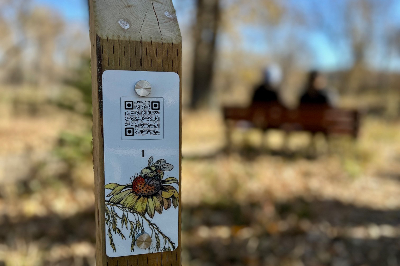 A QR code on a wooden sign post along an outdoor trail.