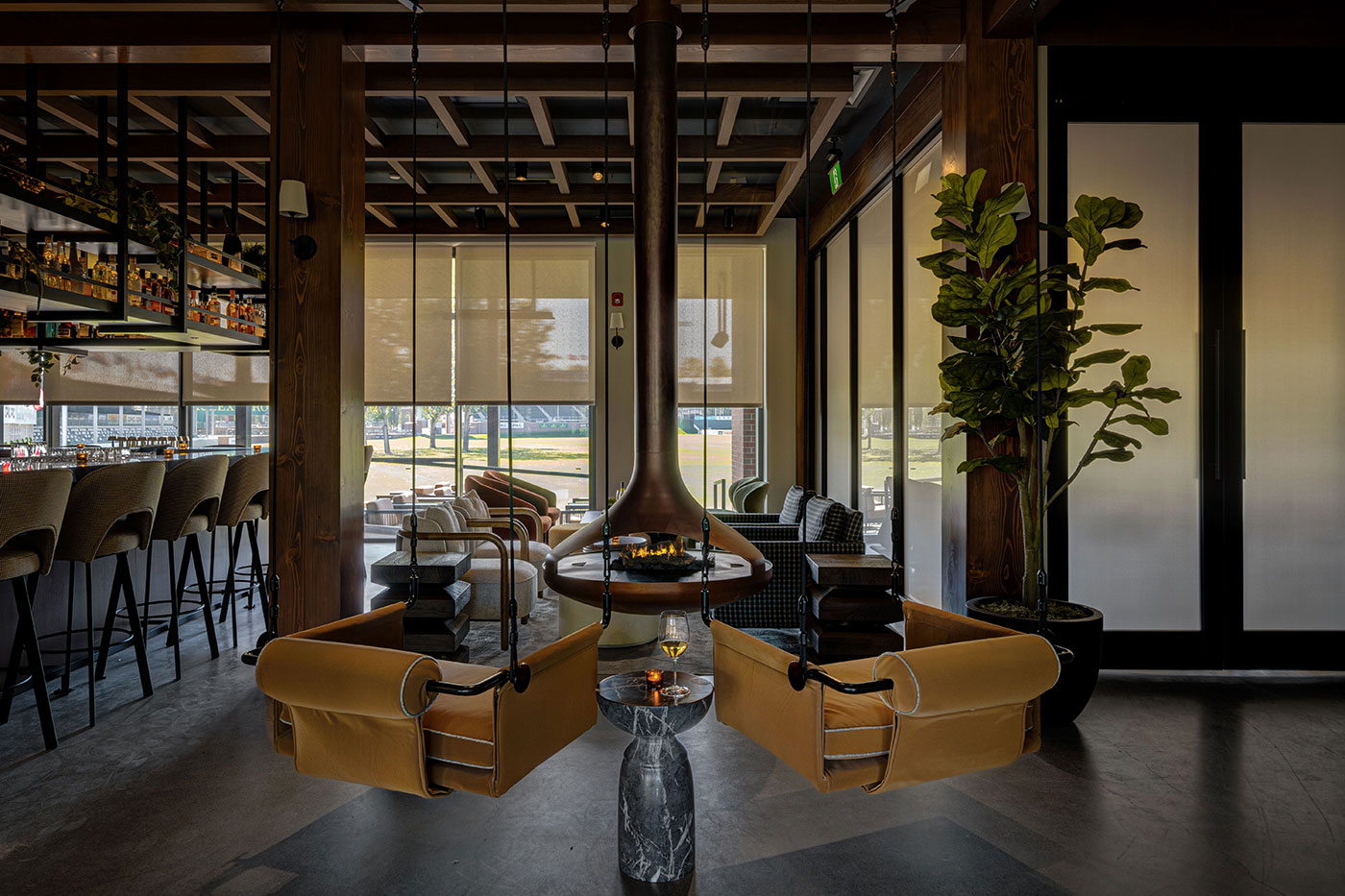 A cozy dining room with a fireplace hanging from the roof surrounded by cozy seating.