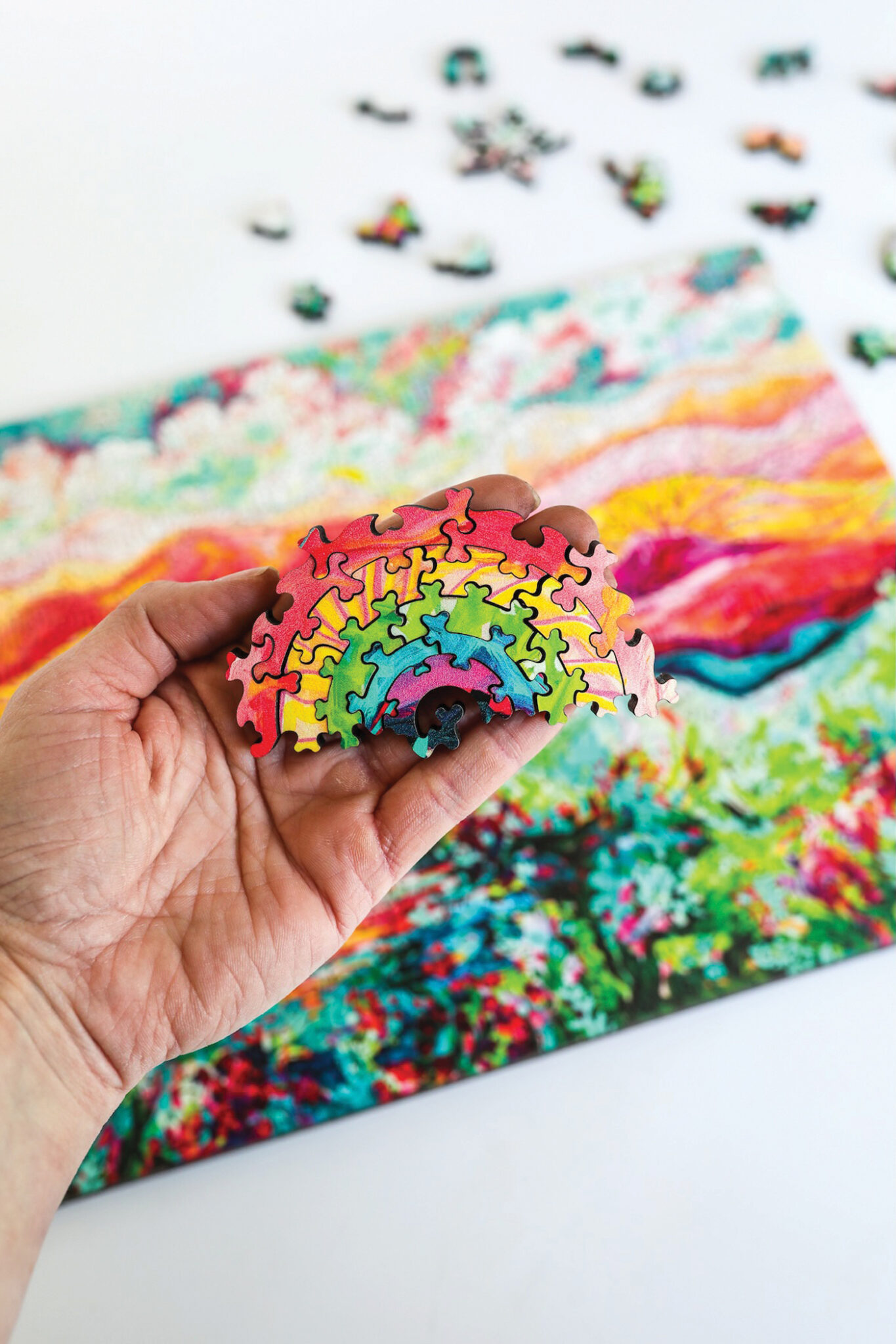 A hand holds some puzzle pieces in the shape of a rainbow
