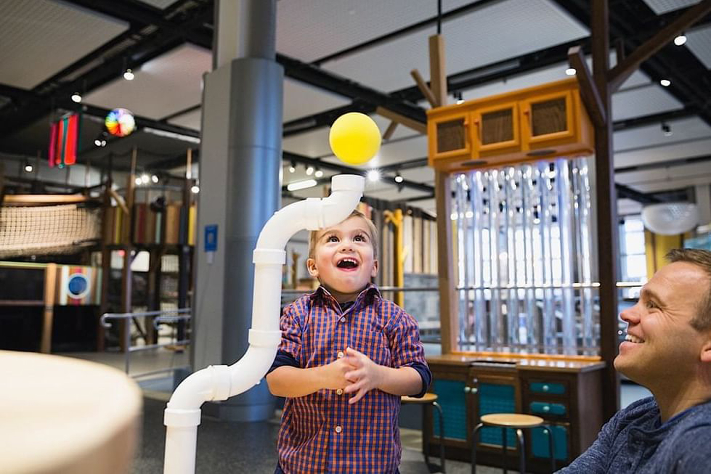 A child and a parent watch a yellow ball floating in the air at a museum