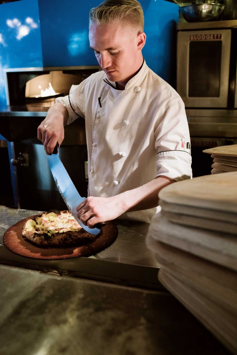 Posto chef Benjamin Mills cutting pizza.