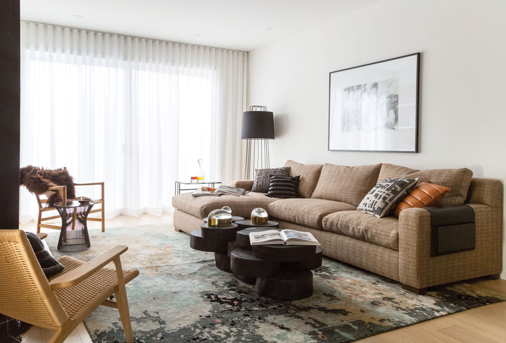 Inky-black and grey tones layered with warm, neutral woods and textiles create the effortless but thoughtful look the homeowner wanted.Sectional sofa from Montauk Sofa; puzzle coffee table from Sanctuary Loft; Jonathan Adler globo boxes on coffee table from Dade Loft; rug from HPR Gallery; living room chairs by Carl Hansen from Le Belle Arti; Knoll Platner end table and Blu Dot perimeter floor lamp from Kit Interior Objects. Ceiling wallpaper throughout from Stewart Drummond Studios; custom drapery throughout the home from RL Design; home builder Dream Master Developments. 