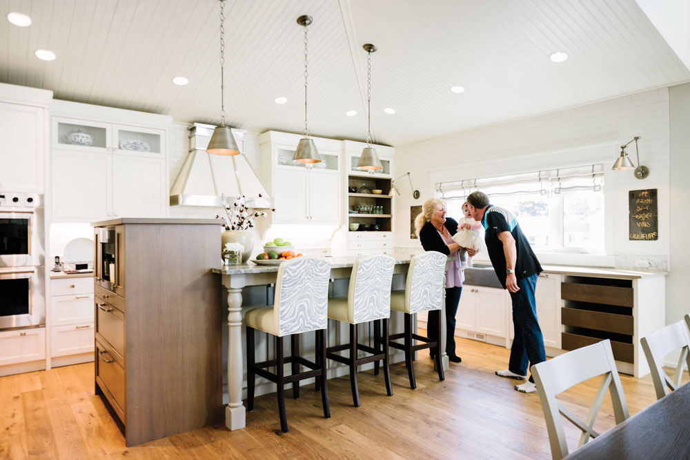 The homeowners play with interior designer Heather Draper’s daughter in the sun-splashed open kitchen, which features custom-made cabinetry by local Crossfield artisans.Lighting, custom drapery, cushions, custom furniture and flooring from The Heather Company. Plumbing fixtures from Robinson Lighting & Bath Centre. Custom millwork by C3 Crossfield Custom Cabinetry. Hardware from Banbury Lane. Countertops from Stone Selection. Wolf and Subzero appliances from Trail Appliances. C2 Paint on walls in Smidgen Kitchen, Cotton Island and Cousteau.